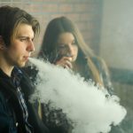 Vape teenagers. Young cute girl in sunglasses and young handsome guy smoke an electronic cigarettes in the vape bar. Bad habit that is harmful to health. Vaping activity.